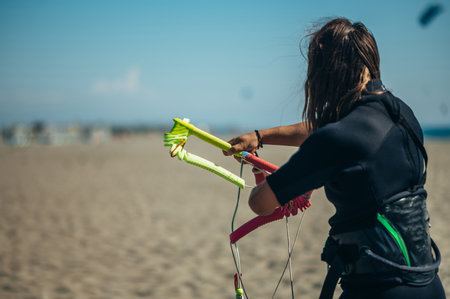 Young sporty woman preparing her equipment for kitesurfing and using flying lines and a control bar...
