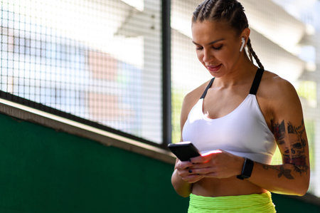 Beautiful attractive woman using smartphone and earphones after finishing her training outside