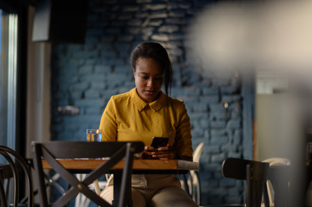 Beautiful young african american woman using a smartphone while sitting in a cafeの写真素材