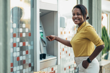 Beautiful young african american woman using an atm machine and a credit card while in the city