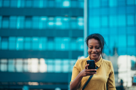 Beautiful young african american woman using a smartphone while sitting on the bench in the cityの写真素材