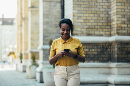 Beautiful young african american woman using a smartphone while walking in the city street