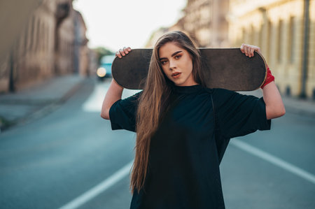 Young woman holding her skateboard and standing on the road in the cityの写真素材