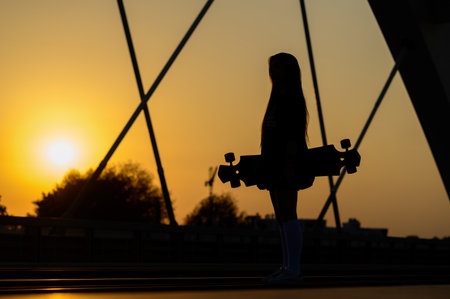 Young woman holding her longboard and standing on the bridgeの写真素材