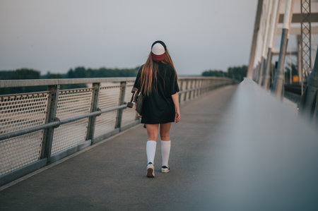Young woman holding her longboard and walking on the bridgeの写真素材