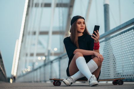Young woman sitting on her longboard and using a smartphone while on the bridgeの写真素材