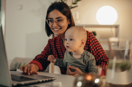 Beautiful business mom using a laptop and smiling while spending time with her cute baby boy at homeの写真素材