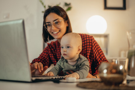 Beautiful business mom using a laptop and smiling while spending time with her cute baby boy at homeの写真素材