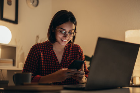 Beautiful woman using smartphone and a laptop while managing her business and working remotely from homeの写真素材
