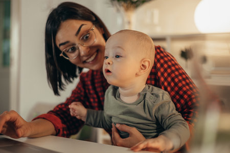 Beautiful business mom using a laptop and smiling while spending time with her cute baby boy at homeの写真素材