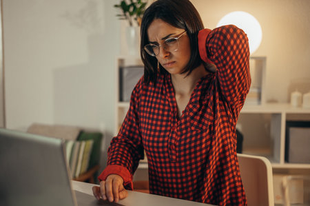 Beautiful woman having back and neck pain while using a laptop and managing her business and working remotely from homeの写真素材