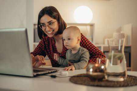 Beautiful business mom using a laptop and smiling while spending time with her cute baby boy at homeの写真素材