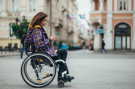 Young beautiful woman with disability who uses a wheelchair using a smartphone while out in the cityの写真素材