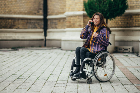 Young beautiful woman with disability who uses a wheelchair using a smartphone while out in the cityの写真素材