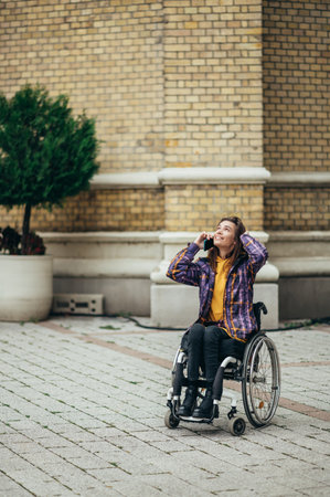 Young beautiful woman with disability who uses a wheelchair using a smartphone while out in the cityの写真素材