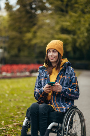 Young beautiful woman in wheelchair using a smartphone while out in the city parkの写真素材
