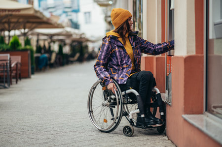 Young beautiful woman with disability who uses a wheelchair using credit card and atm machine while withdrawing moneyの写真素材