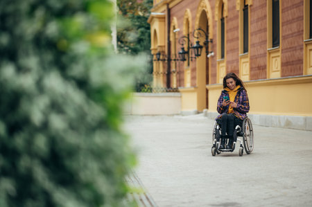 Young beautiful woman with disability who uses a wheelchair using a smartphone while out in the cityの写真素材