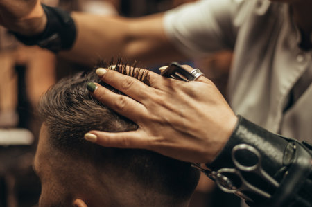 Young man getting haircut by hairdresser while sitting in chair at barbershopの写真素材