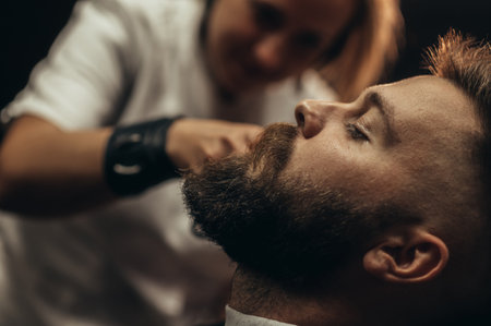 Young bearded man getting beard haircut by hairdresser at barbershopの写真素材