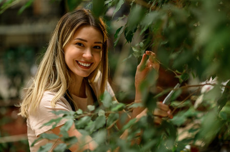 Beautiful young florist taking care of a plant while using pruning shears and working in a flower...