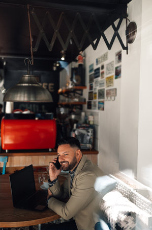 Handsome businessman using a smartphone and working on his laptop while drinking coffee in a cafeの写真素材