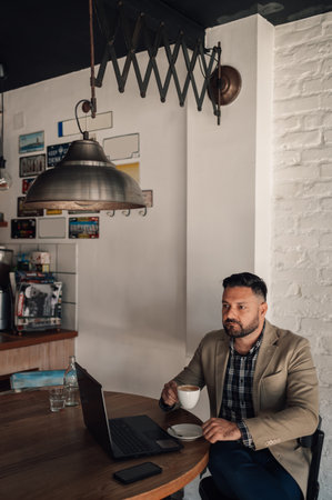 Handsome businessman working on his laptop while drinking coffee in a cafeの写真素材