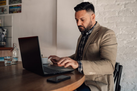 Handsome businessman working on his laptop while drinking coffee in a cafeの写真素材