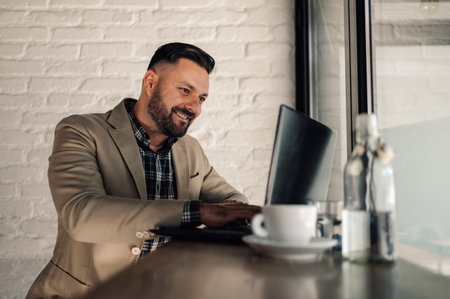 Handsome businessman working on his laptop while drinking coffee in a cafeの写真素材