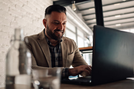 Handsome businessman working on his laptop while drinking coffee in a cafeの写真素材