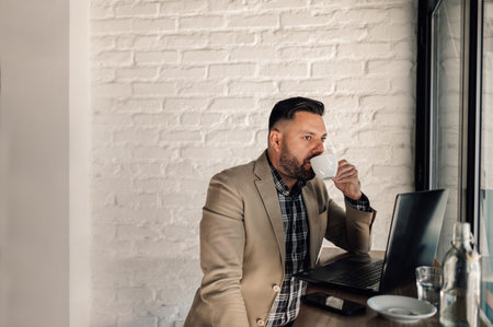 Handsome businessman working on his laptop while drinking coffee in a cafeの写真素材
