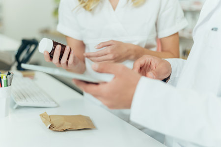 Close shot of a male and female colleagues pharmacist hands holding a bottle of medicine and a tablet while working in a pharmacyの写真素材