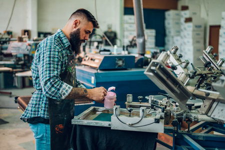 Male worker pressing ink on frame while using the printing machine in a workshopの写真素材