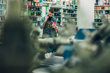 Male worker mixing colors for screen printing in a workshop and using a smartphoneの写真素材