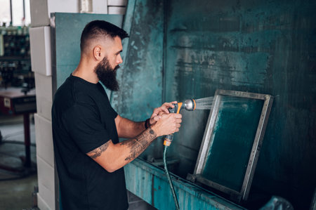 Male worker cleaning screen frame with water in a printing workshopの写真素材