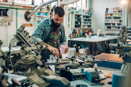 Male worker pressing ink on frame while using the printing machine in a workshopの写真素材