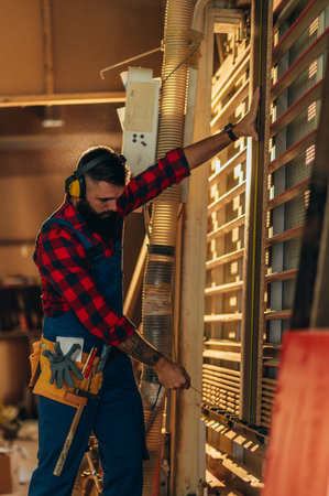 Young male carpenter working in workshop and wearing safety earphoneの写真素材