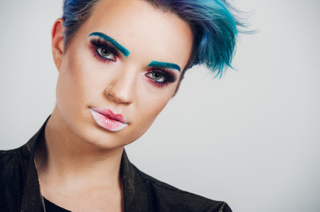 Portrait of an authentic beautiful woman with colorful makeup looking into the at camera against the against white background. Perfect fresh clean skin. Blue hair color.の写真素材