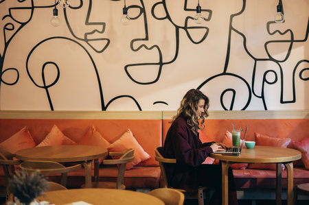 Beautiful young woman drinking coffee and working on her laptop in a cafeの写真素材
