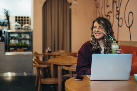 Beautiful young woman drinking matcha latte coffee and working on her laptop in a cafeの写真素材
