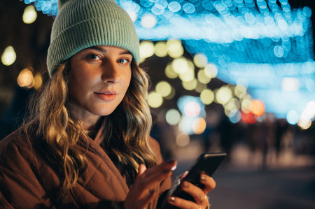Young woman using a smartphone outside with the city lights in the backgroundの写真素材