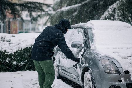 Man cleaning snow from the car after a heavy snowfall. Middle aged man removing snow from car with brush and scraper tool. A car covered with snow.の写真素材