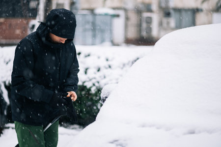 Man cleaning snow from the car after a heavy snowfall. Middle aged man removing snow from car with...