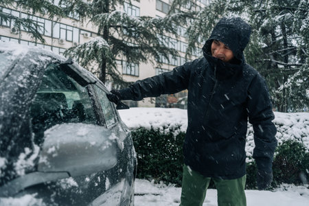 A man cleaning the car from the snow with special brushes and scraper tool. Cold snowy and frosty morning. Middle aged man cleaning car covered with snow.の写真素材