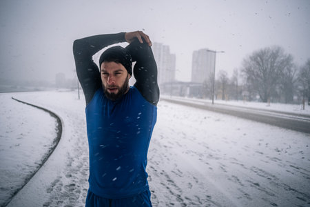Handsome male stretching before training outside while it is snowing on a cold winter day....