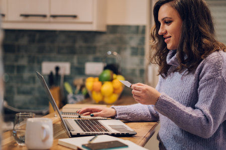 Young hispanic woman shopping online using laptop and credit card in a cozy decorated apartment. Online payments. Easy pay using digital gadget.の写真素材