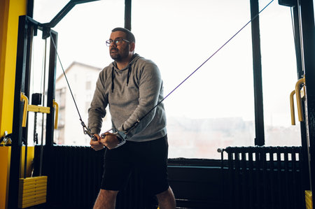 Obese middle aged men training in the gym with the help of a personal instructor and using a cross...