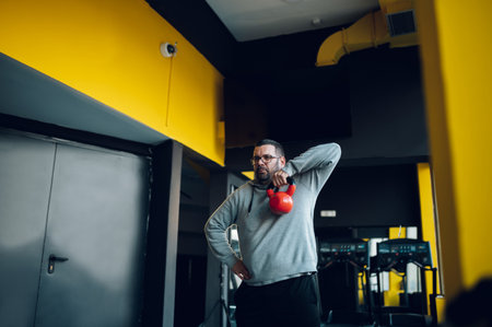 Fat middle aged men using kettlebell while exercising at the gym. Overweight man trying to reduce...