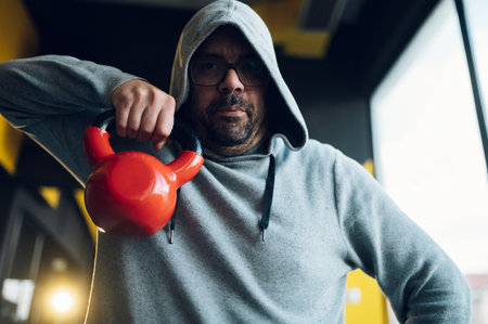 Fat middle aged men using kettlebell while exercising at the gym. Overweight man trying to reduce weight. Obese man doing fitness exercises.の写真素材