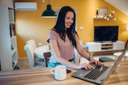 Smiling middle aged woman using laptop in the kitchen at home. Home office.の写真素材